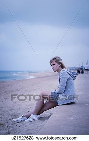Stock Photo - Young woman sitting on sea wall, looking out to sea. Fotosearch