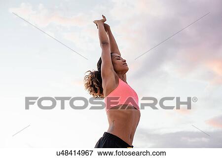 Stock Photo - Young woman stretching arms on beach, Tuscany, Italy. Fotosearch