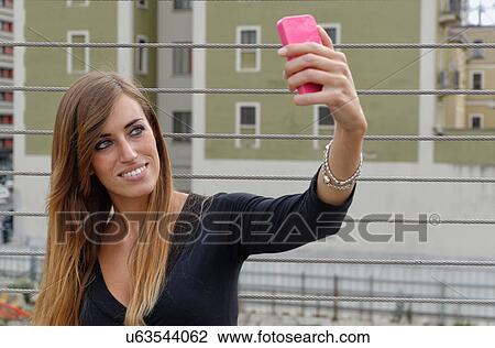 Stock Image - Young woman taking self portrait using smartphone. Fotosearch