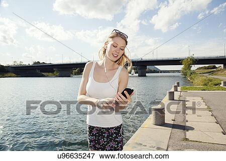 Stock Photo - Young woman texting on smartphone on Danube Island riverside, Vienna, Austria. Fotosearch