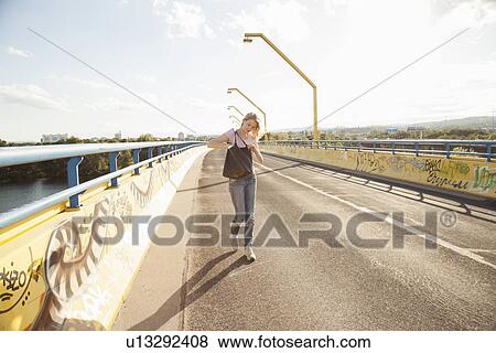 Stock Photo - Young woman walking across bridge looking in shoulder bag. Fotosearch