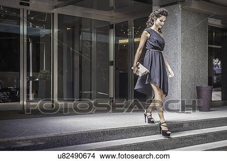 Picture - Young woman wearing black dress going down steps. Fotosearch