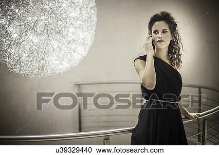 Stock Image - Young woman wearing black dress on cell phone, portrait. Fotosearch