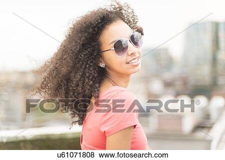 Young woman wearing sunglasses looking over shoulder View Large Photo Image Stock Photo - Young woman wearing sunglasses looking over shoulder. Fotosearch