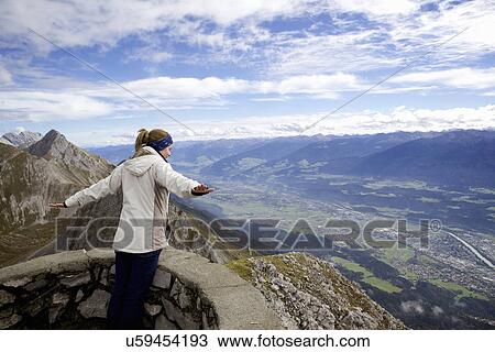 Stock Image - Young woman with arms open on top of mountain, Innsbruck Tyrol, Austria. Fotosearch