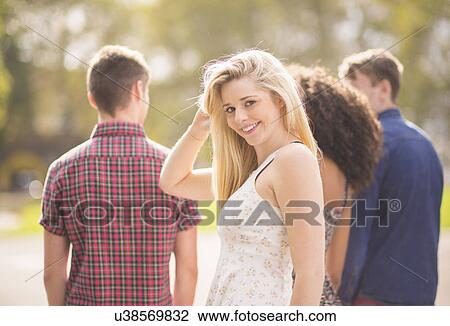 Stock Image - Young woman with friends in park looking over her shoulder. Fotosearch