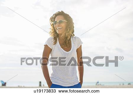 Stock Image - Young woman with hands in pockets on beach, Tuscany, Italy. Fotosearch