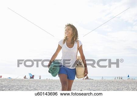 Stock Photograph - Young woman with towel and beach bag on beach, Tuscany, Italy. Fotosearch