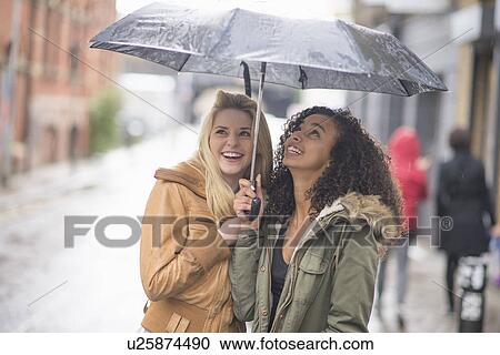 Stock Image - Young women sheltering under umbrella. Fotosearch
