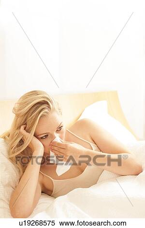 Stock Photography - Woman in bed blowing nose on tissue. Fotosearch