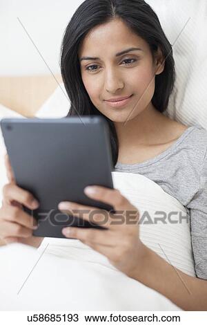 Stock Image - Woman in bed using digital tablet. Fotosearch