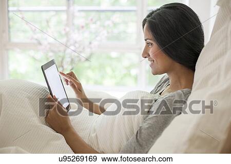 Stock Photo - Woman in bed using digital tablet. Fotosearch