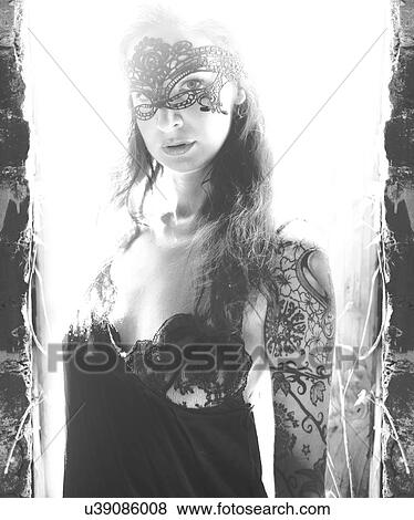 Stock Photo - Tattooed woman with mask in front of window. Fotosearch