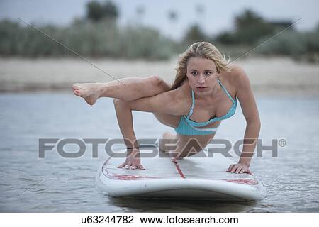 Stock Image - Young woman exercising on surfboard. Fotosearch