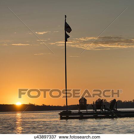 Adirondack chairs and flag on a dock at sunset, Lake of The Woods, Ontario, Canada View Large Photo Image Stock Photo - Adirondack chairs and flag on a dock at sunset, Lake of The Woods, Ontario, Canada. Fotosearch
