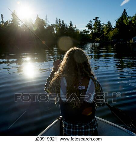 Stock Image - Girl on boat in a lake at morning sunlight, Lake of The Woods, Kenora, Lake of The Woods, Ontario, Canada. Fotosearch