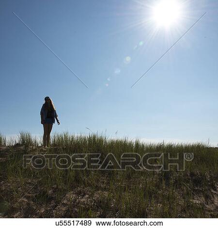 Stock Photo - Girl standing on grassy sand dune under bright sunshine at Cavendish Dunelands Trail, Green Gables, Prince Edward Island, Canada. Fotosearch