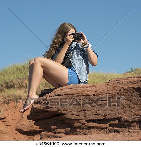 Stock Image - Girl taking a picture on a rock, Cavendish Beach, Green Gables, Prince Edward Island, Canada. Fotosearch