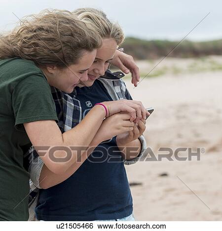 Stock Photograph - Girls watching smartphone on the beach, York Point, Prince Edward Island, Canada. Fotosearch