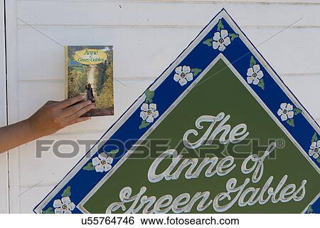 Stock Photograph - Person holding book beside Anne of Green Gables sign on wall, Avonlea, Green Gables, Prince Edward Island, Canada. Fotosearch