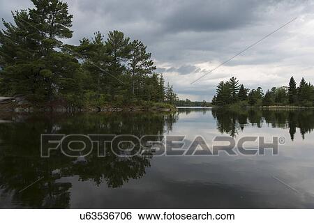 Stock Photograph - Reflection of trees and clouds in a lake, Lake of The Woods, Ontario, Canada. Fotosearch