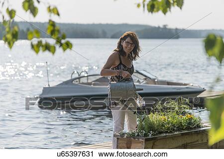 Stock Image - Woman watering plants on a dock, Lake of The Woods, Ontario, Canada. Fotosearch