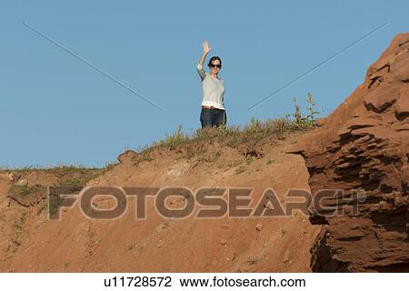 Stock Image - Woman waving from top of rocky cliff, Green Gables, Cavendish, Prince Edward Island, Canada. Fotosearch