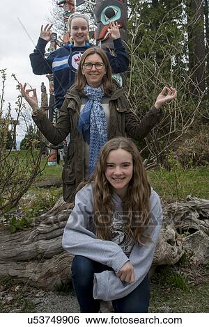 Stock Photograph - Woman with her daughters posing in front of totem poles at Stanley Park, Vancouver, British Columbia, Canada. Fotosearch