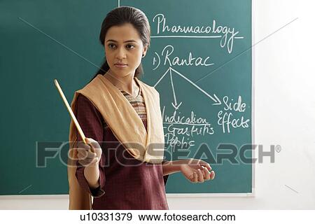 Stock Photo - An angry female teacher holding ruler against green board . Fotosearch