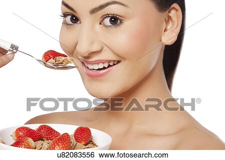 Stock Photograph - An attractive young woman eating cornflakes with strawberries . Fotosearch