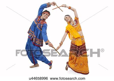 Stock Photograph - An Indian couple in traditional wear performing Dandiya Raas over white background. Fotosearch