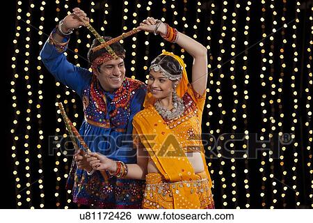 An Indian couple in traditional wear performing Dandiya Raas against neon lights View Large Photo Image Stock Photograph - An Indian couple in traditional wear performing Dandiya Raas against neon lights. Fotosearch