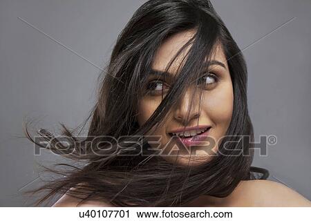Stock Image - Attractive young female with hair blowing over face against colored background . Fotosearch