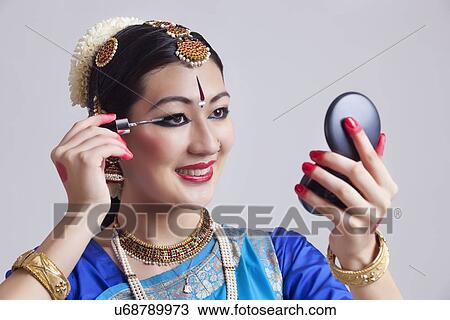 Stock Image - Beautiful Bharatanatyam dancer applying mascara over gray background. Fotosearch