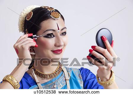 Stock Photo - Beautiful Bharatanatyam dancer applying mascara over gray background. Fotosearch