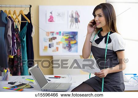 Stock Photograph - Beautiful fashion designer holding sketch on phone in studio . Fotosearch