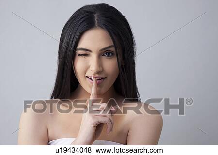 Stock Photo - Beautiful winking woman gestures for silence over colored background . Fotosearch