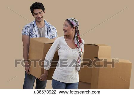 Stock Image - Beautiful young couple carrying cardboard boxes together while moving in . Fotosearch