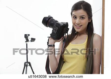 Beautiful young female holding camera against white background View Large Photo Image Stock Photo - Beautiful young female holding camera against white background . Fotosearch