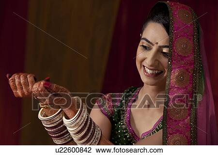 Stock Image - Beautiful young Indian bride looking at her bangles . Fotosearch