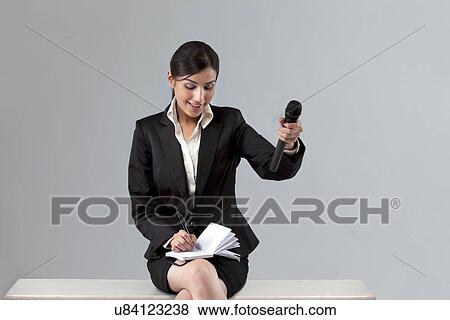 Stock Photo - Beautiful young reporter asking comment while writing in notepad against colored background . Fotosearch