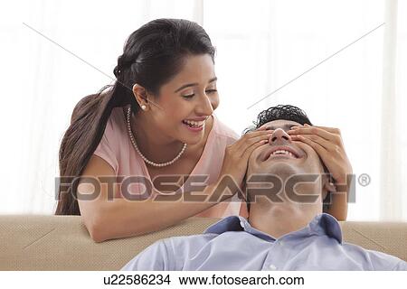 Beautiful young woman covering man's eyes at home View Large Photo Image Picture - Beautiful young woman covering man's eyes at home . Fotosearch