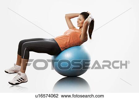 Stock Image - Beautiful young woman doing abdominal exercise on a fitness ball over white background . Fotosearch