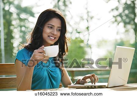 Beautiful young woman having cup of coffee while using laptop View Large Photo Image Stock Image - Beautiful young woman having cup of coffee while using laptop . Fotosearch