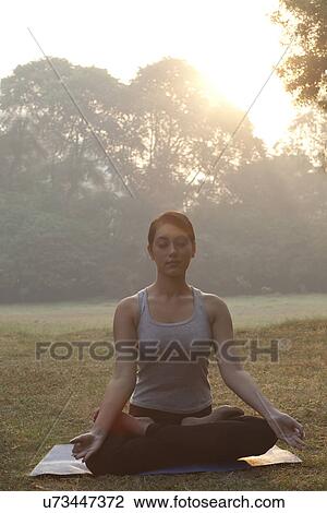 Stock Image - Beautiful young woman meditating in park . Fotosearch