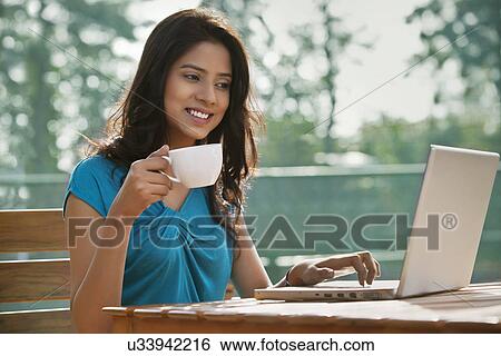 Beautiful young woman using laptop while having coffee View Large Photo Image Stock Photograph - Beautiful young woman using laptop while having coffee . Fotosearch