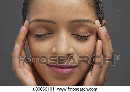 Stock Image - Beautiful young woman with her eyes closed and fingers on temples . Fotosearch