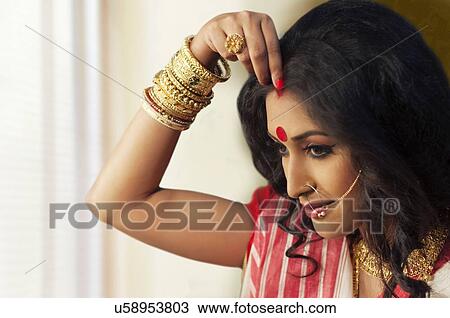 Stock Image - Bengali woman putting sindoor on her forehead. Fotosearch