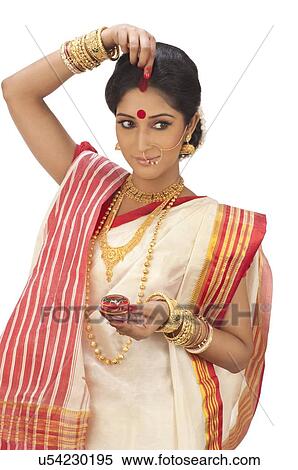 Stock Photography - Bengali woman putting sindoor on her forehead. Fotosearch