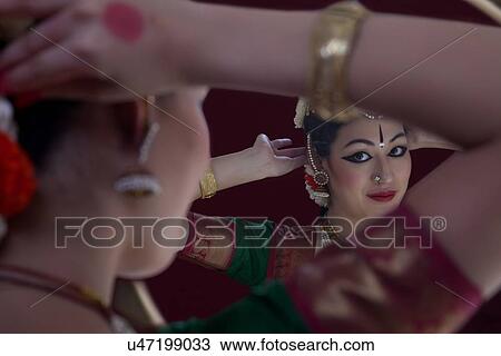Stock Image - Bharatanatyam dancer getting dressed in front of mirror over black background. Fotosearch